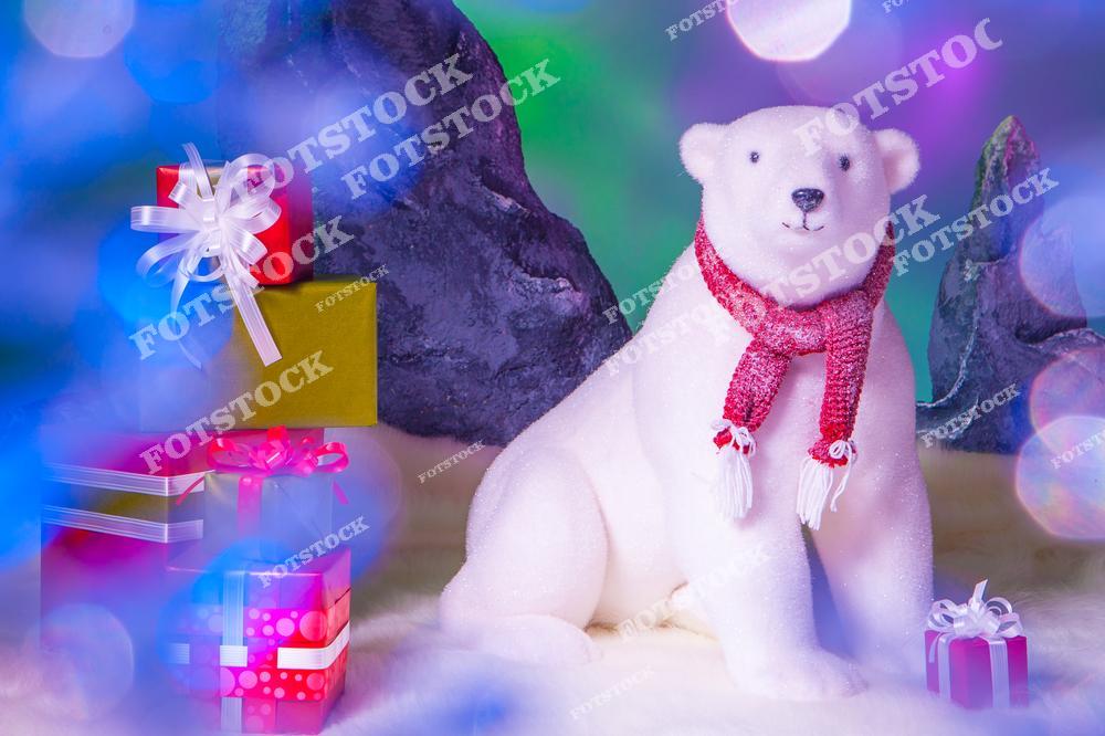 На фотографии изображена декоративная фигурка белого медведя в красном шарфе, окруженная празднично упакованными подарками. Фон и мягкое освещение создают ощущение зимней сказки и праздничного настроения. Композиция передает атмосферу зимней сказки и новогодних чудес.